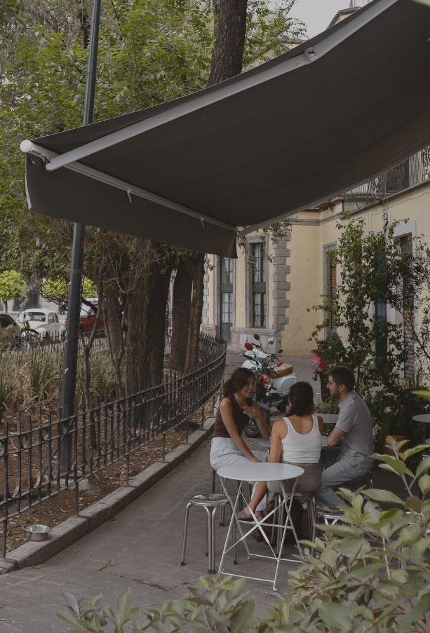 Personas disfrutando terraza de café bajo toldo retráctil oscuro en colonia de Ciudad de México